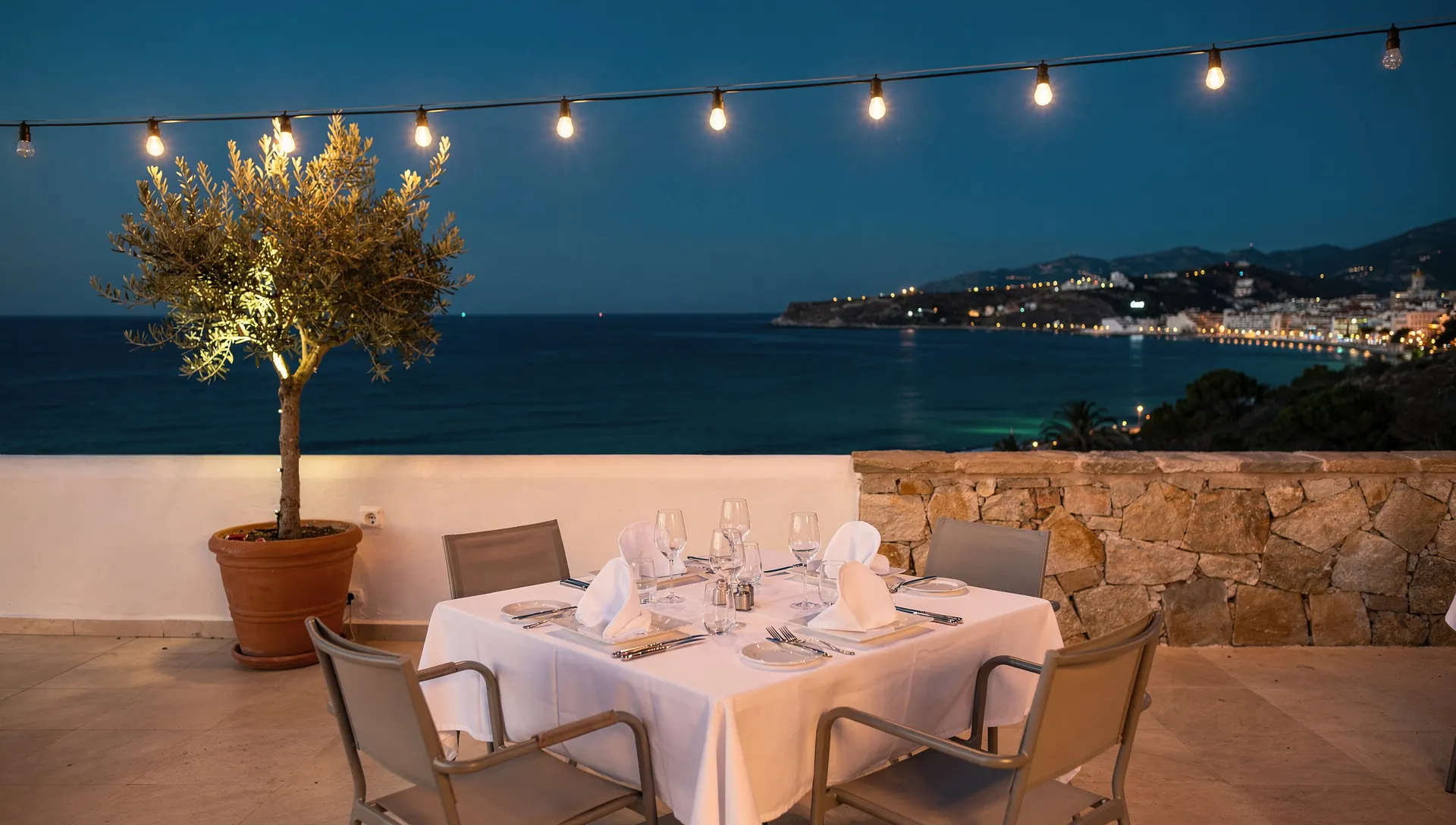 A candlelit table for two on a terrace above the bay just after sunset