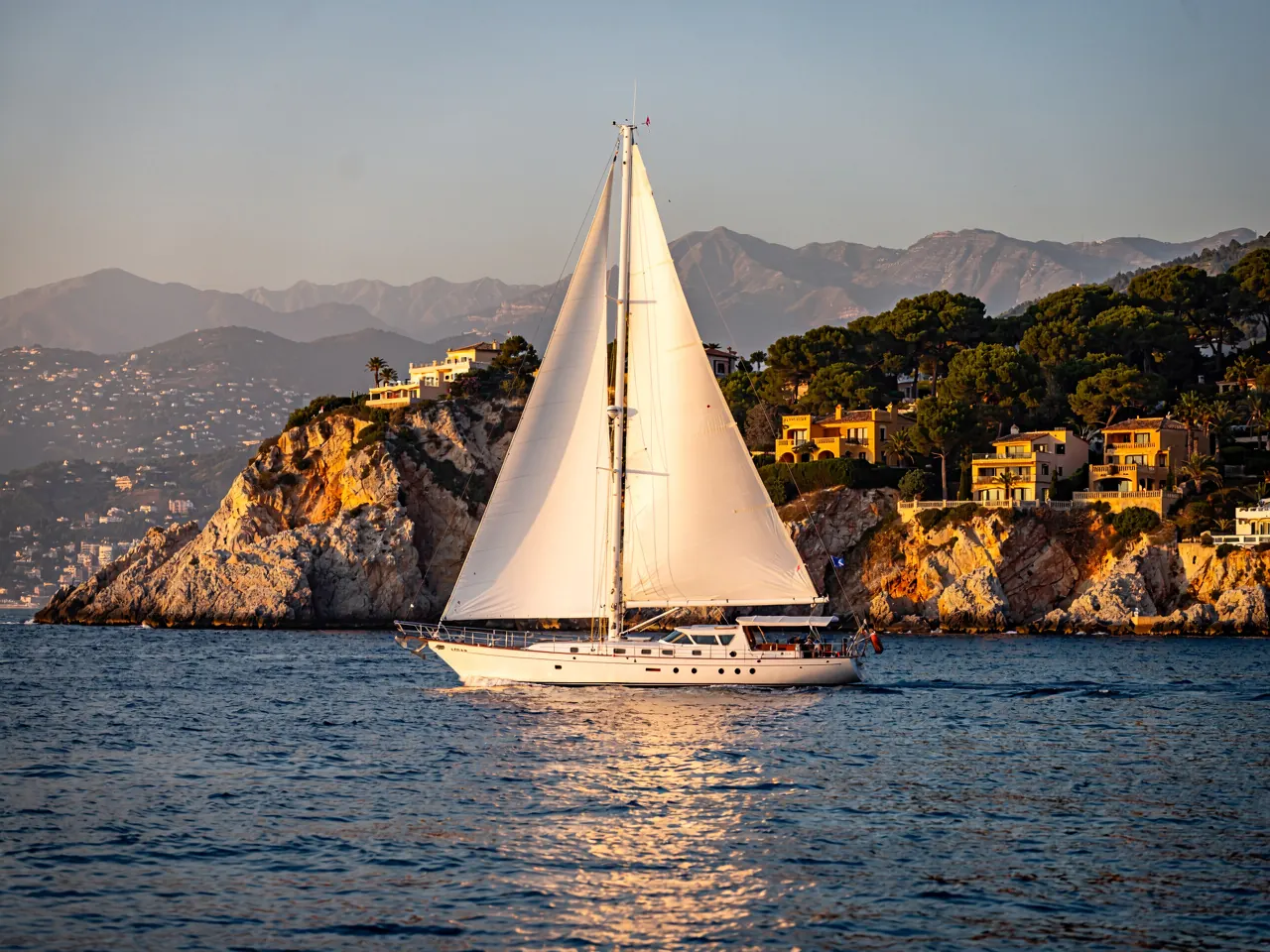 A sailing yacht under sail along the coast in late afternoon