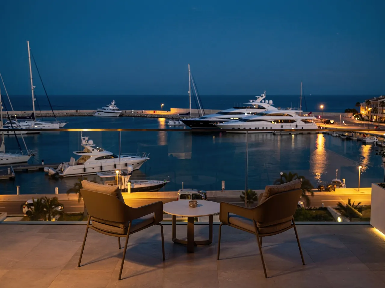 An apartment balcony over a marina with yachts in the blue hour