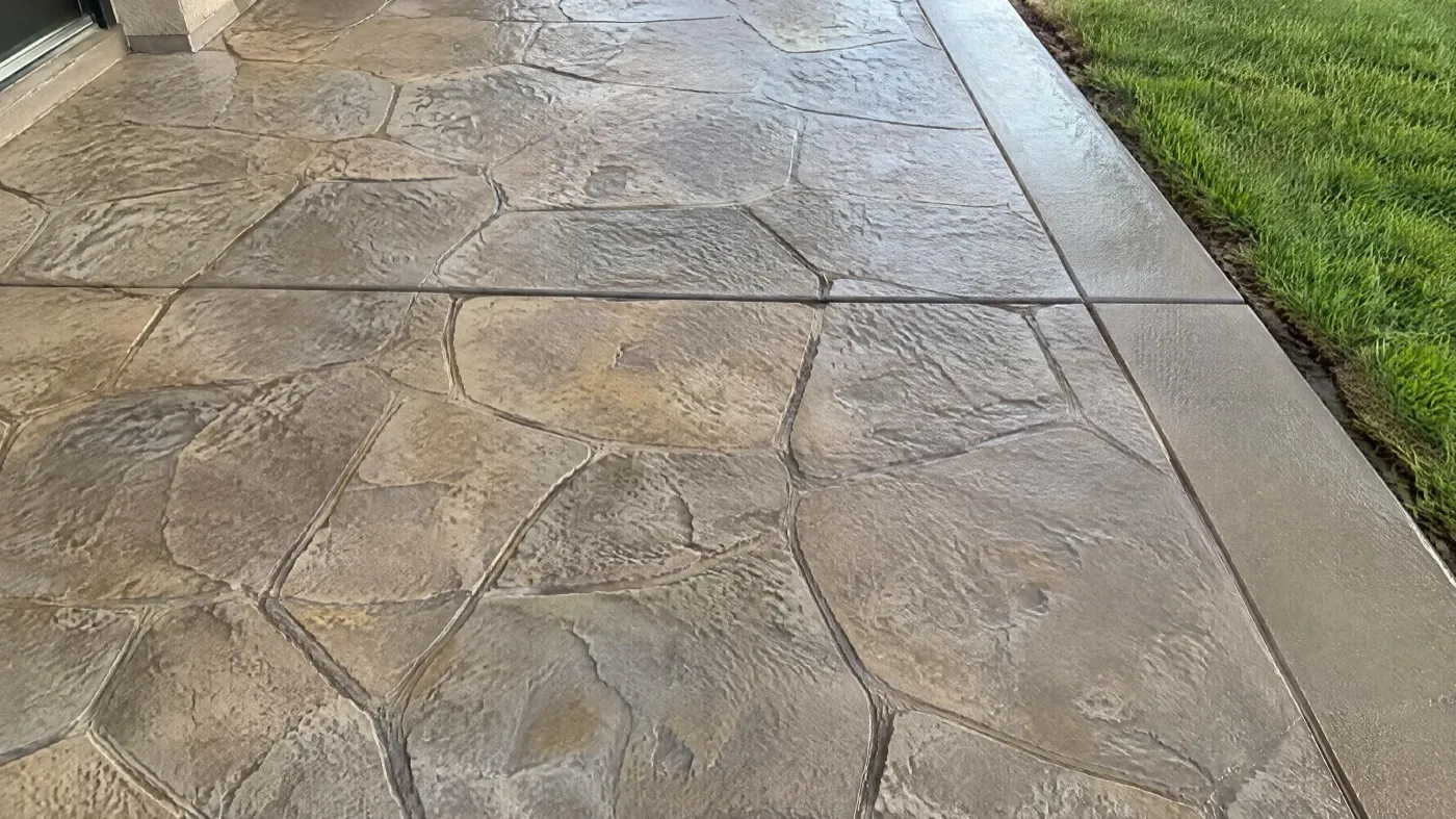 Terrasse en béton imprimé motif pierre, joint de retrait scié et bordure lisse le long du gazon