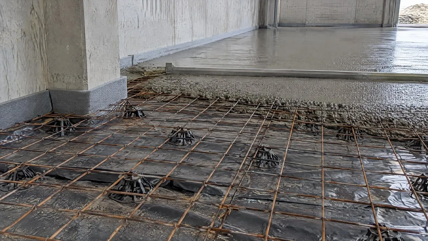Treillis soudé posé sur cales au-dessus du film polyéthylène, joint d'isolement au pied d'un poteau, béton en cours de réglage au fond