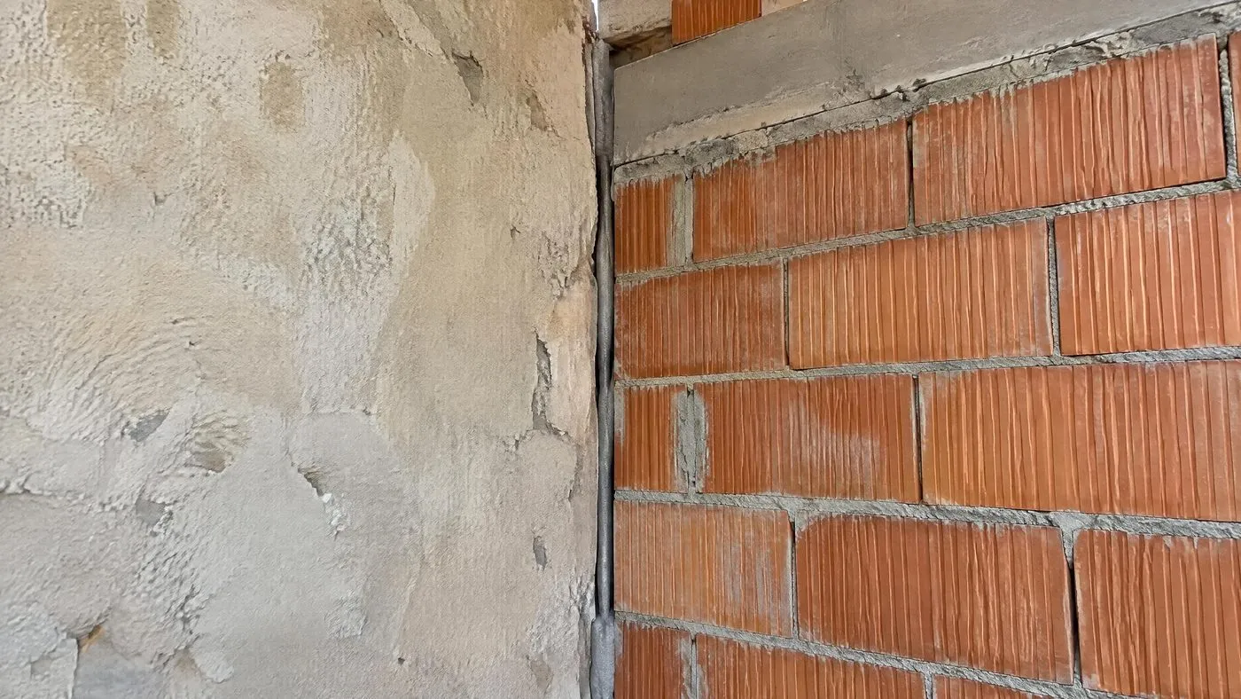 Jonction verticale entre le mur enduit d'une maison et le mur en briques d'une extension, séparés par un joint continu