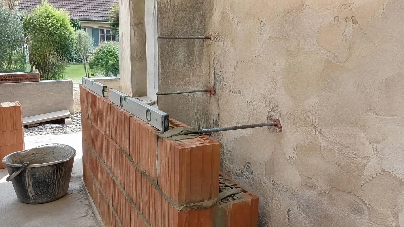 Armatures en attente scellées dans le mur d'une maison, à l'alignement d'un mur en briques en cours de montage