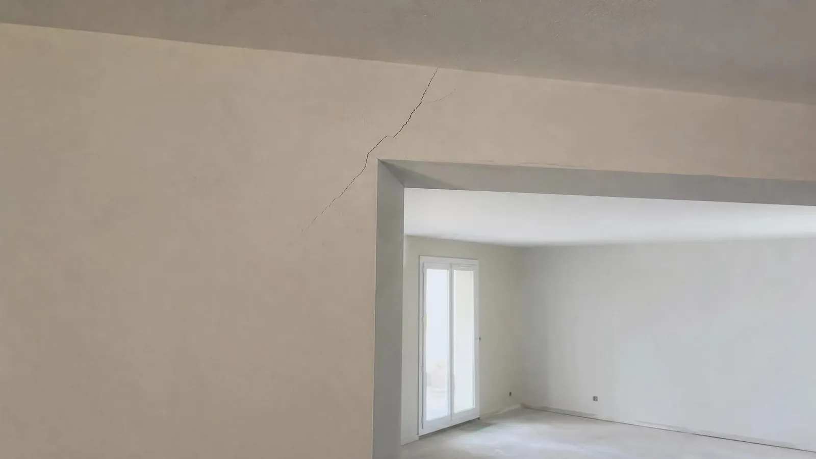 Fissure en diagonale partant de l'angle haut d'une ouverture dans un mur enduit