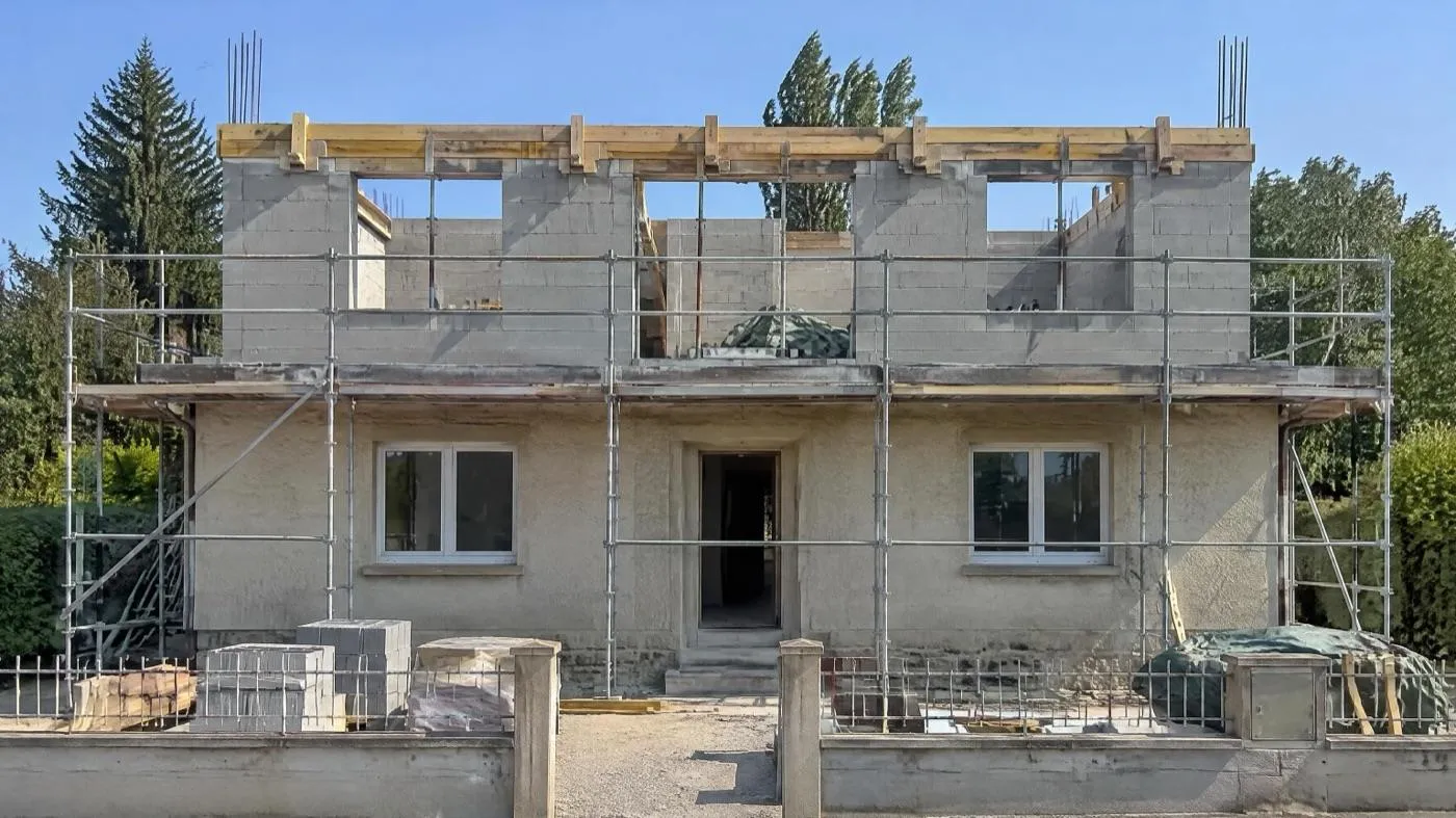 Maison des années 1960 dont la toiture a été déposée, nouveau niveau en blocs béton en cours de montage, aciers en attente aux angles, échafaudage
