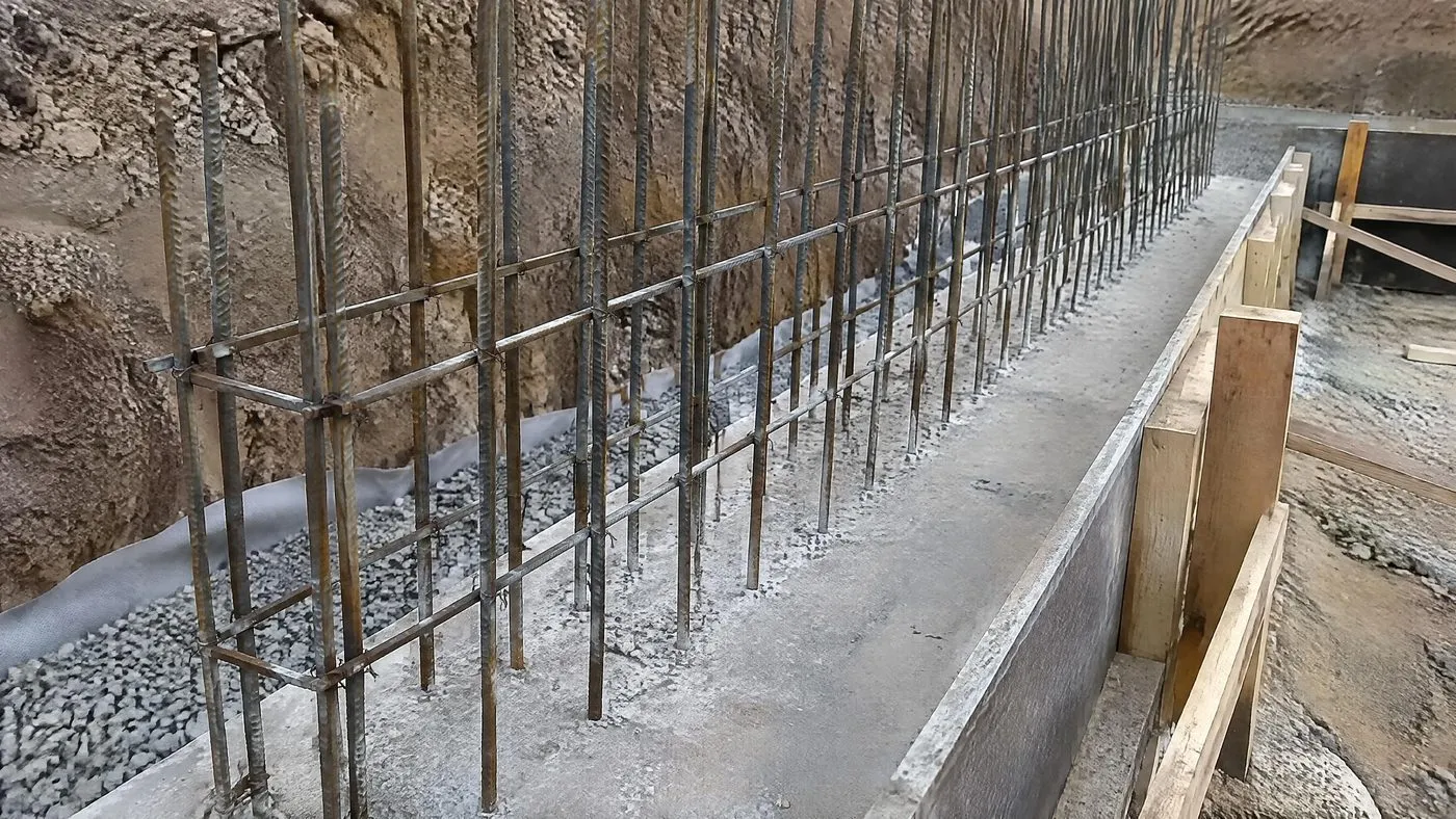 Semelle de mur de soutènement coulée, aciers verticaux en attente sur deux rangs, massif drainant et géotextile contre le talus
