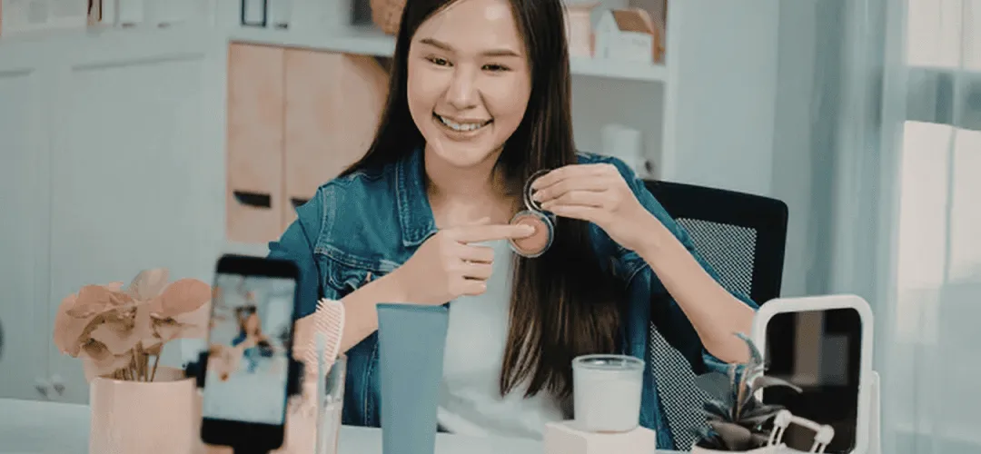 A girl sitting at a desk making a TikTok video about makeup.