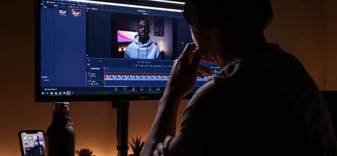 A person edits a video on a dark, dimly lit desk setup.