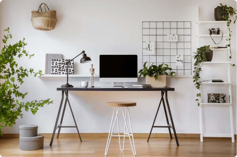 Minimalist home office with a dark trestle desk, iMac, desk lamp, and plants in a bright, airy room.