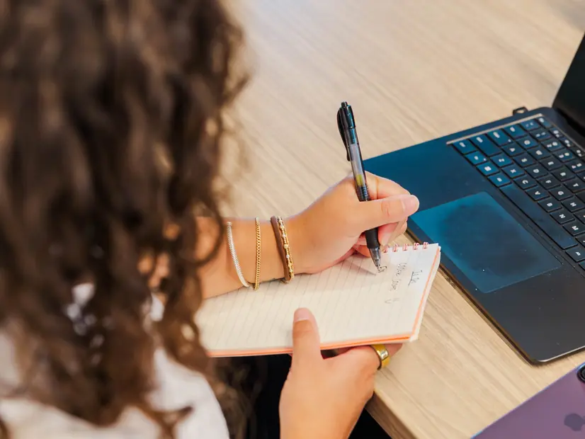 A team member writing in a notebook next to a laptop