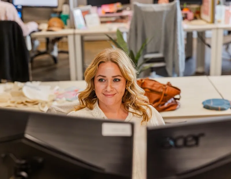 A smiling woman at her computer in an open-plan office