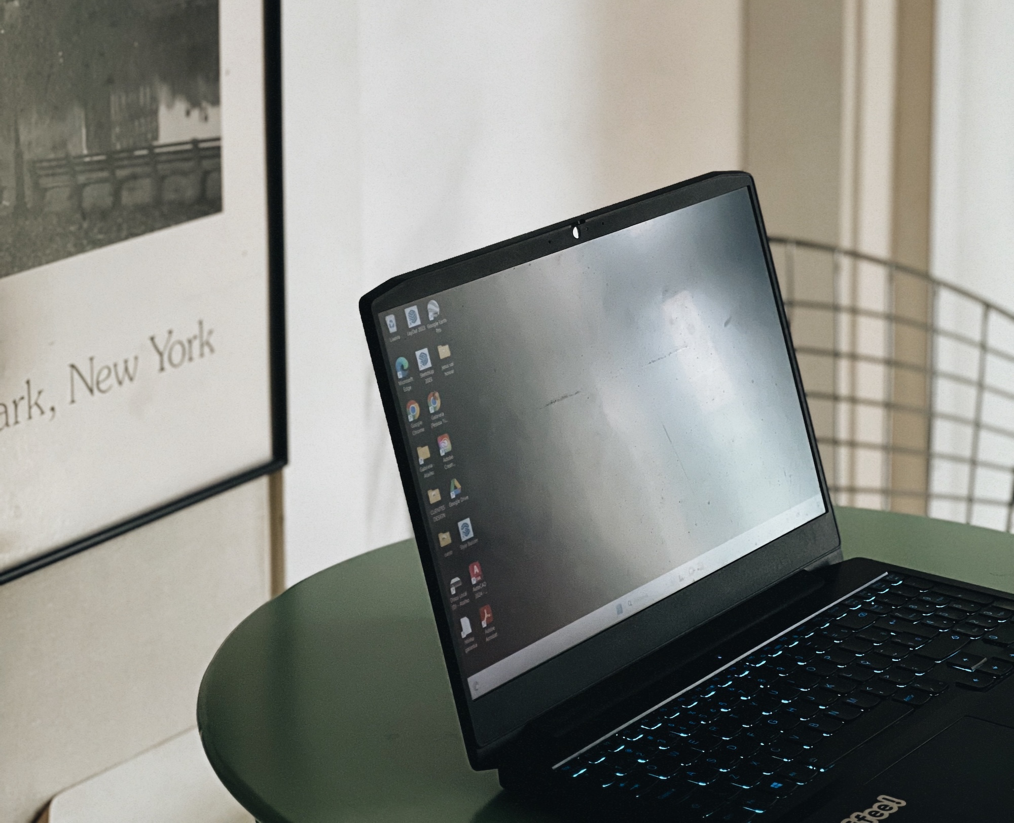 Laptop open on a small green table beside a framed New York print