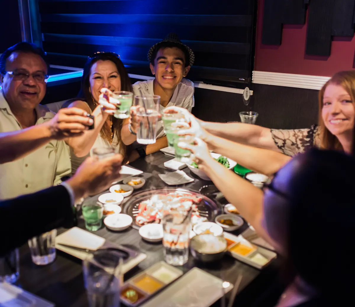 Friends raising soju glasses in a toast at a GEN table