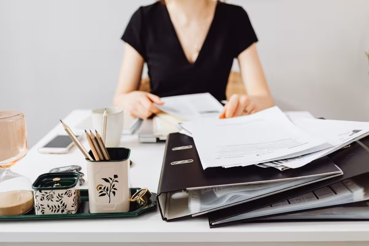 Schreibtisch voller Ordner und Unterlagen, an dem eine Frau arbeitet