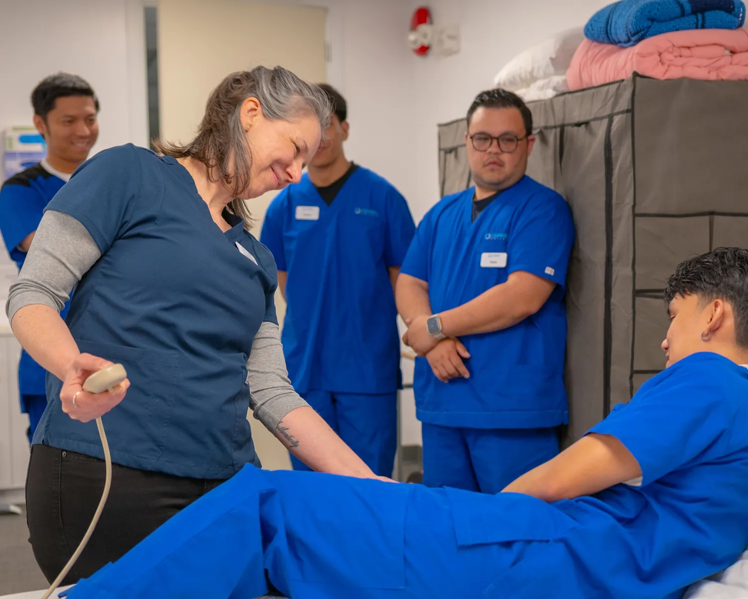An instructor demonstrates a care skill as a group of nurses in scrubs looks on.