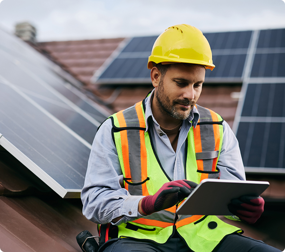 An installer on a roof with solar panels, using a tablet