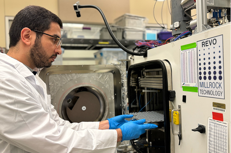 Researcher in a lab coat and gloves loading a tray into a Millrock REVO freeze dryer