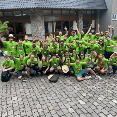 Group of about 35 people wearing matching green shirts posing enthusiastically outdoors on cobblestone pavement in front of a building.