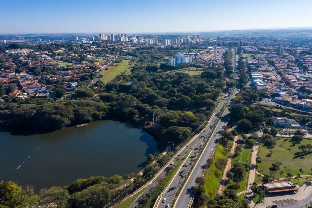 Aerial view of a city featuring a large park with dense trees and a lake alongside a multi-lane road with vehicle traffic.