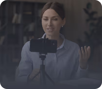 Woman recording a video using a smartphone mounted on a tripod, gesturing with her hand.