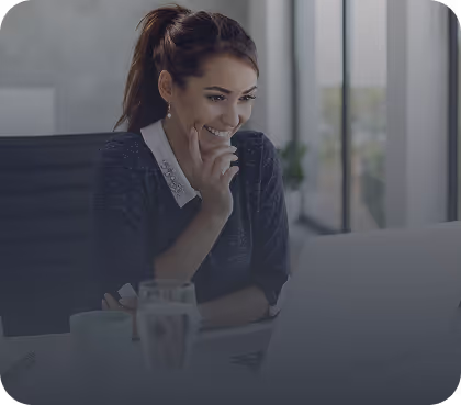 Smiling woman with ponytail working on a laptop in a bright office.