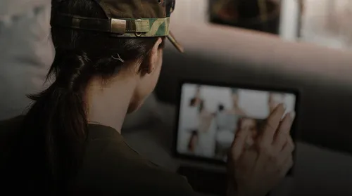 Person wearing a camouflage cap and dark shirt engaging in a video call on a tablet.