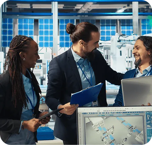 Three professionals smiling and discussing work in a modern industrial or tech setting with robotic equipment and computer screens.