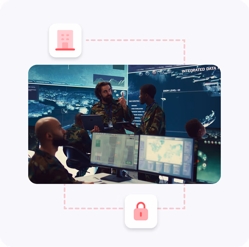 Military personnel in camouflage uniforms working in a command center with multiple computer monitors and digital maps displayed on large screens.