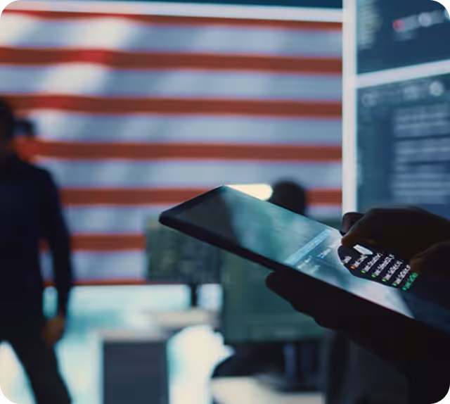 Person holding a tablet with a blurred American flag and people in the background.