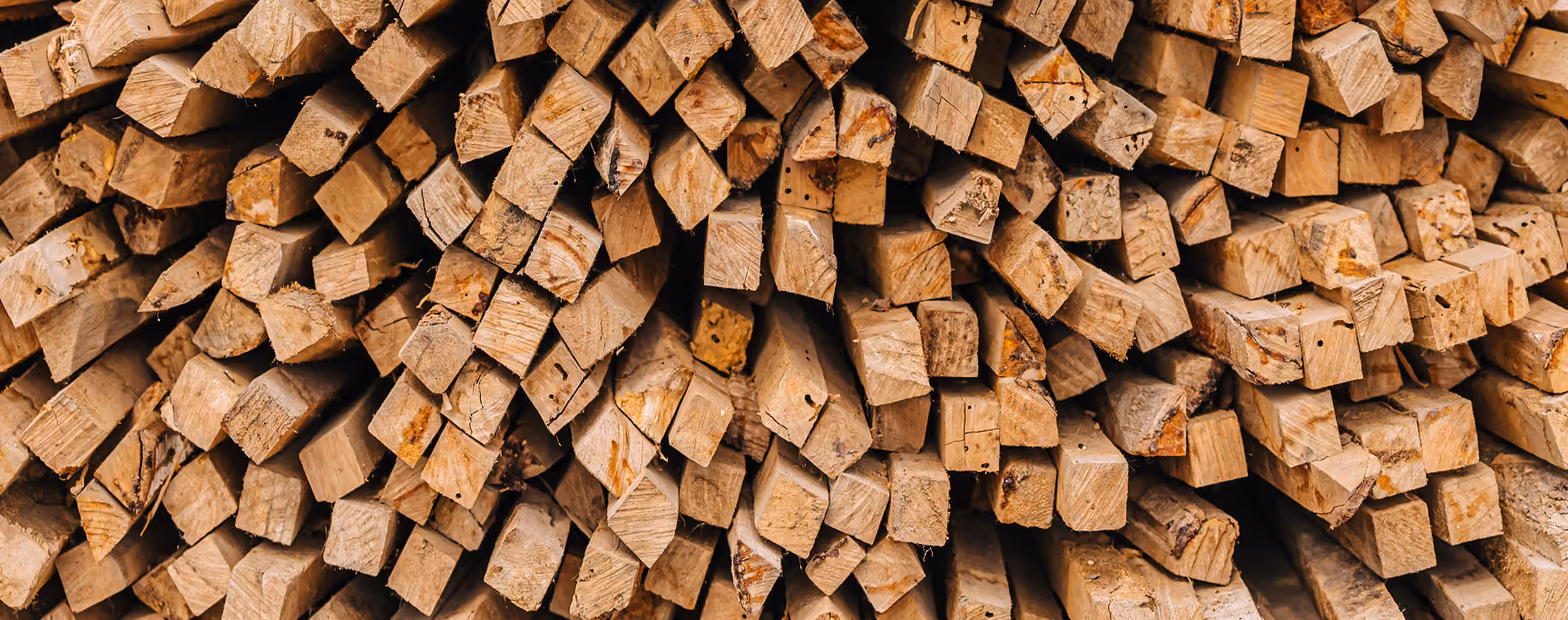Stack of cut, square wooden beams arranged closely, showing their rough cut ends and natural wood grain.