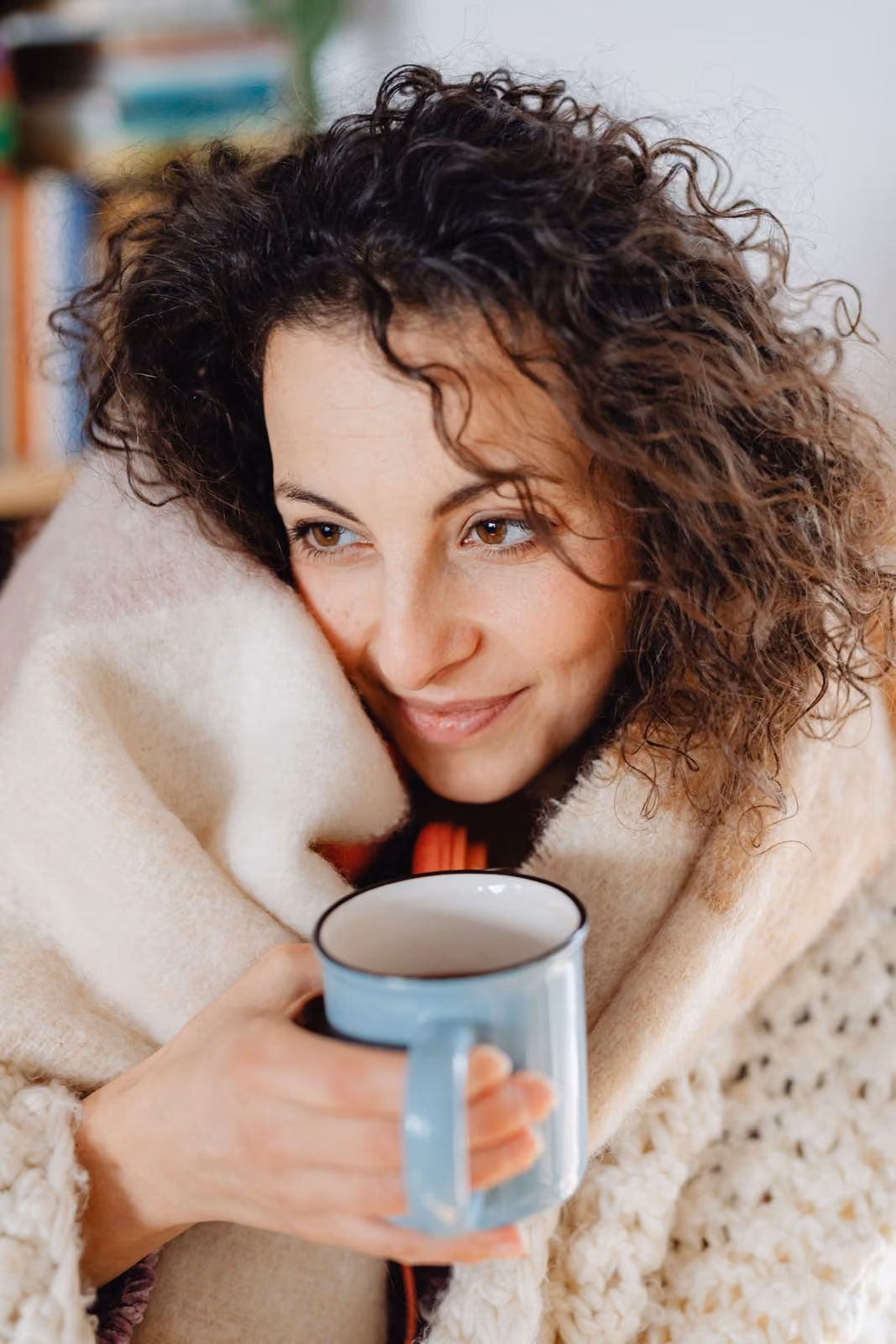 A woman wrapped in a blanket holding a mug, smiling softly