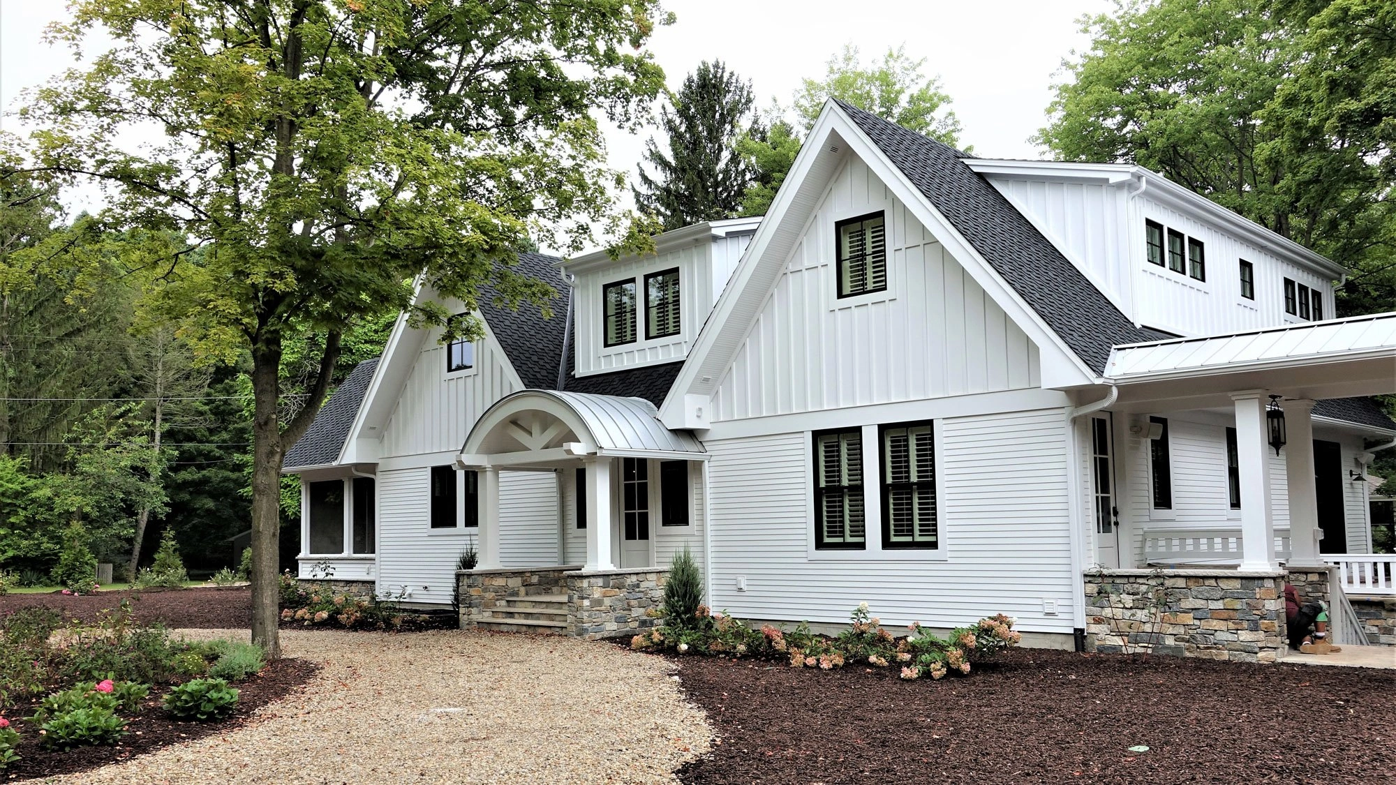 At Home in Harbert residence with white board-and-batten siding, steep gables, black windows, and landscaped grounds