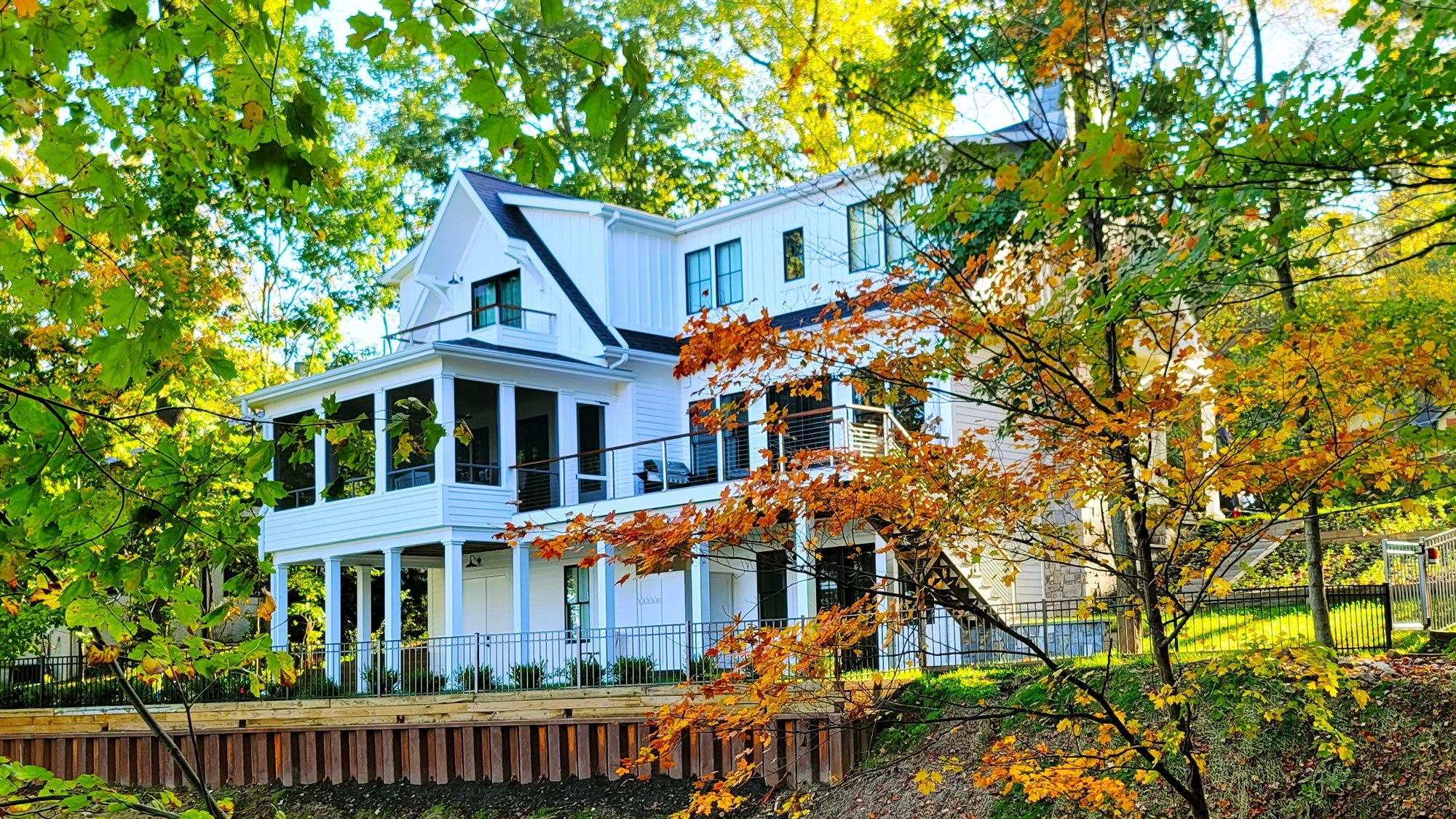 Lakeside House — white lake house with layered porches framed by autumn foliage
