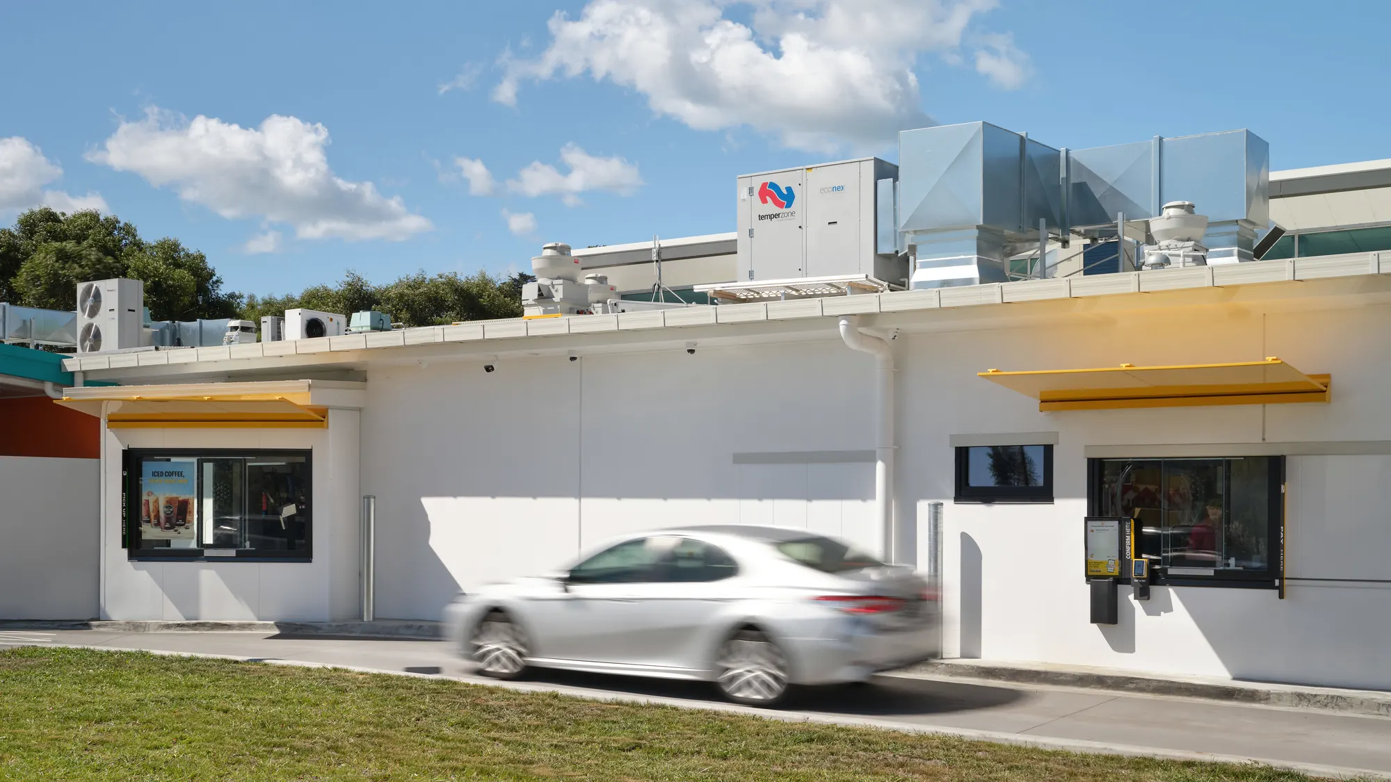 Two yellow canopies along the drive-through wall, with a car passing