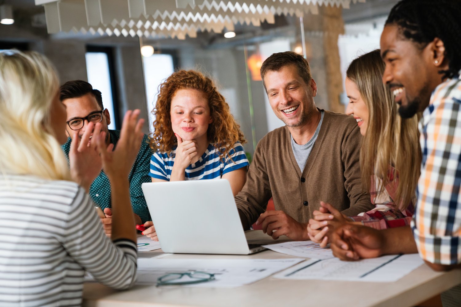Groep collega's lacht rond een laptop aan een tafel