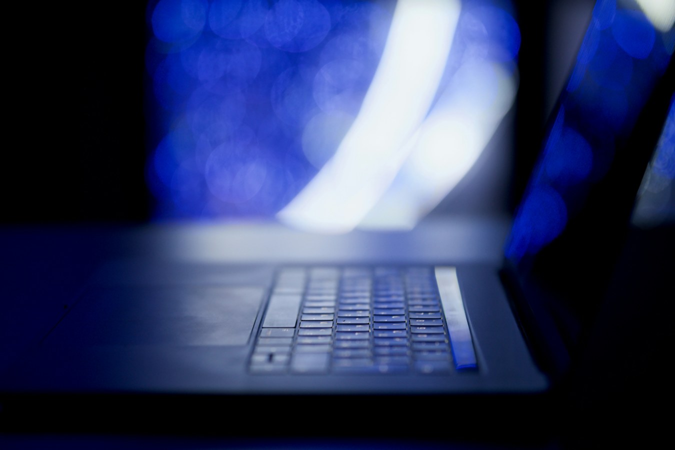 Laptoptoetsenbord in het donker met blauwe lichtvlekken op de achtergrond