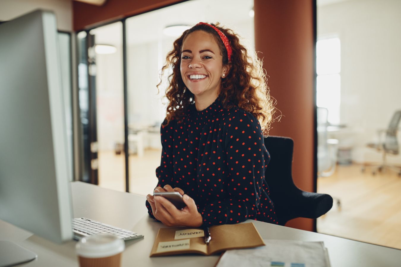 Vrouw met krullend haar houdt telefoon vast naast een computerscherm