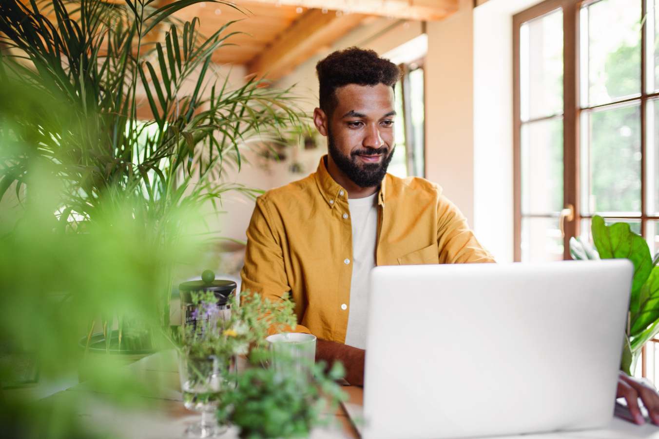 Man in geel shirt werkt op een laptop tussen kamerplanten