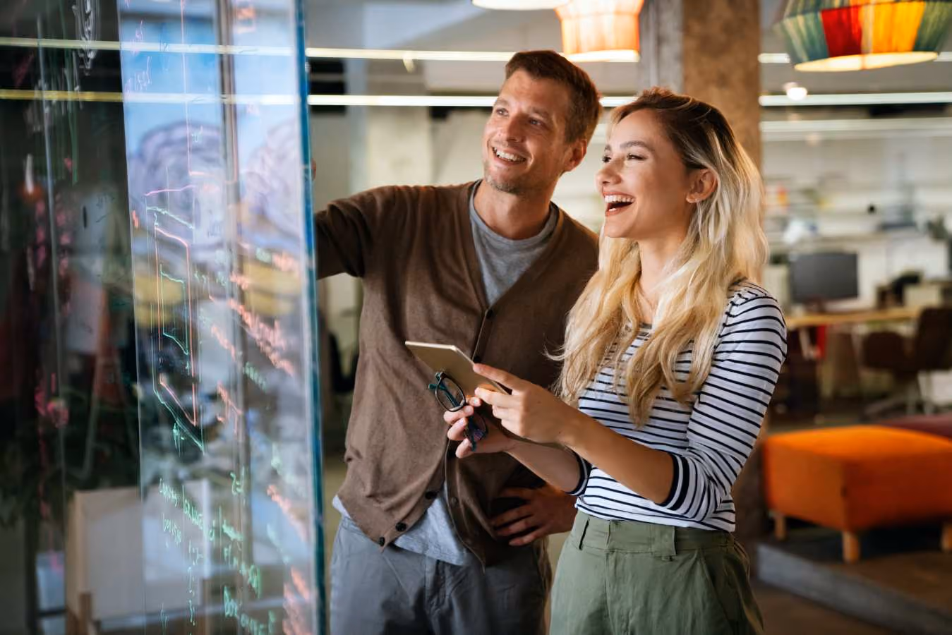 Man en vrouw kijken samen lachend naar digitaal scherm op kantoor
