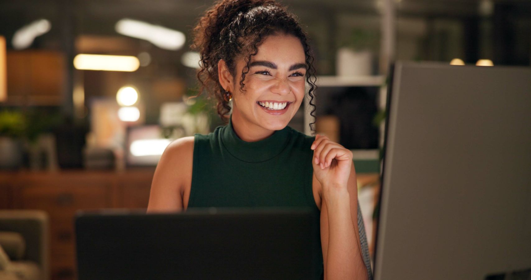 Laughing woman behind a laptop and computer screen in a dimly lit room