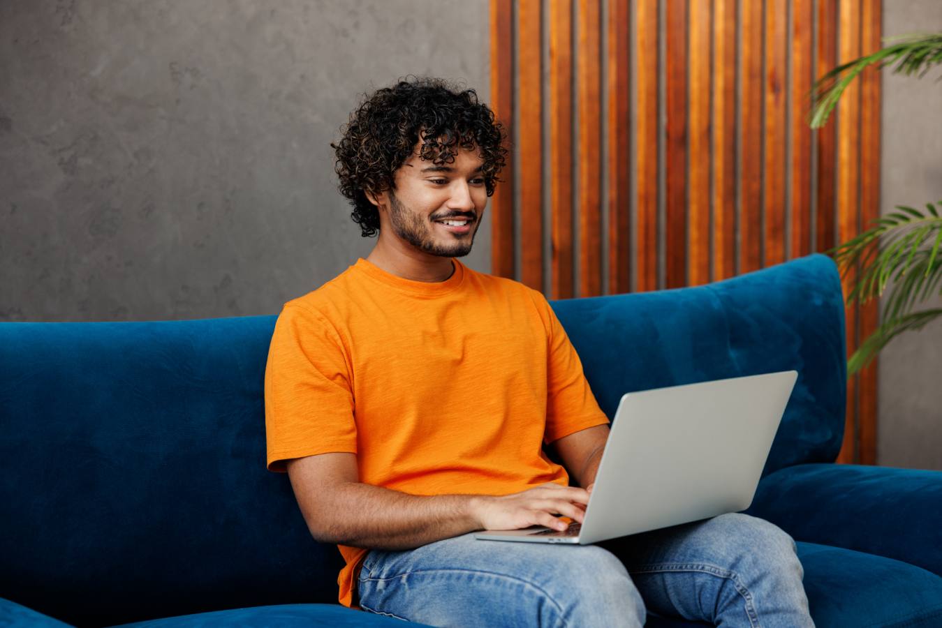 Young man in an orange shirt working on a laptop on a blue sofa