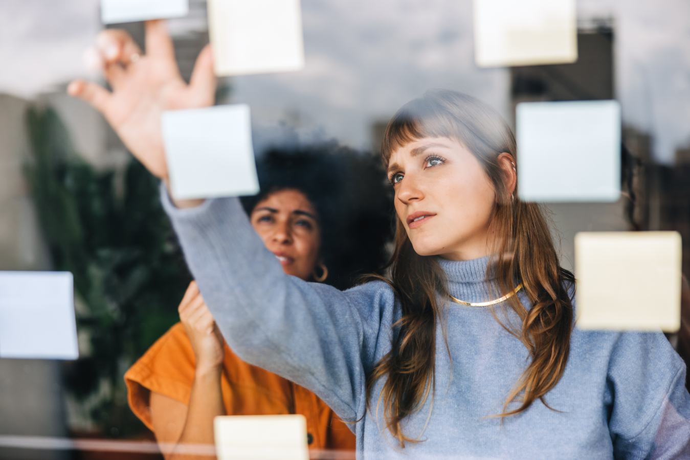 Twee vrouwen plakken gele memoblaadjes op een glazen wand