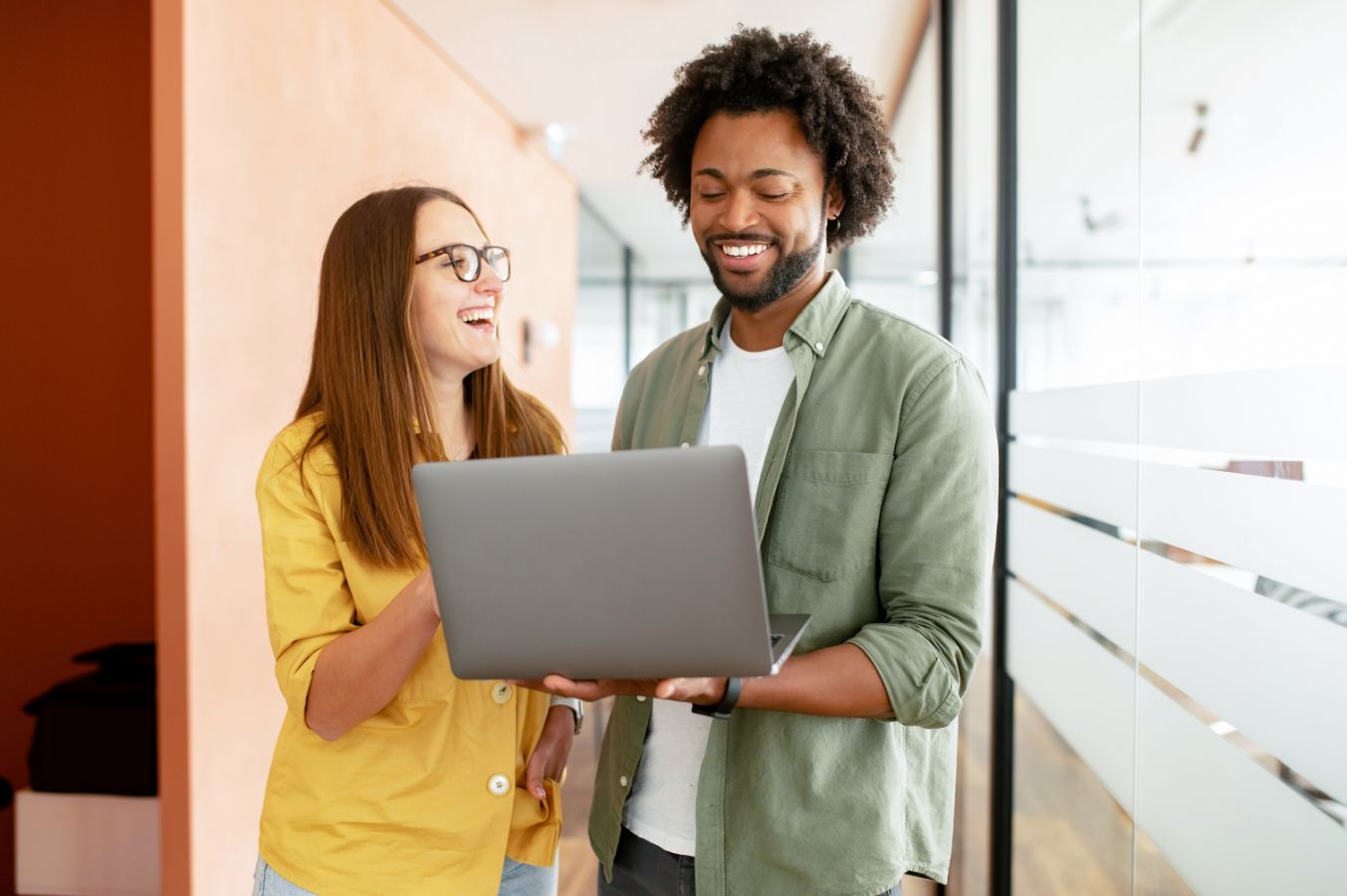Lachend duo bekijkt samen een laptop in kantoorgang
