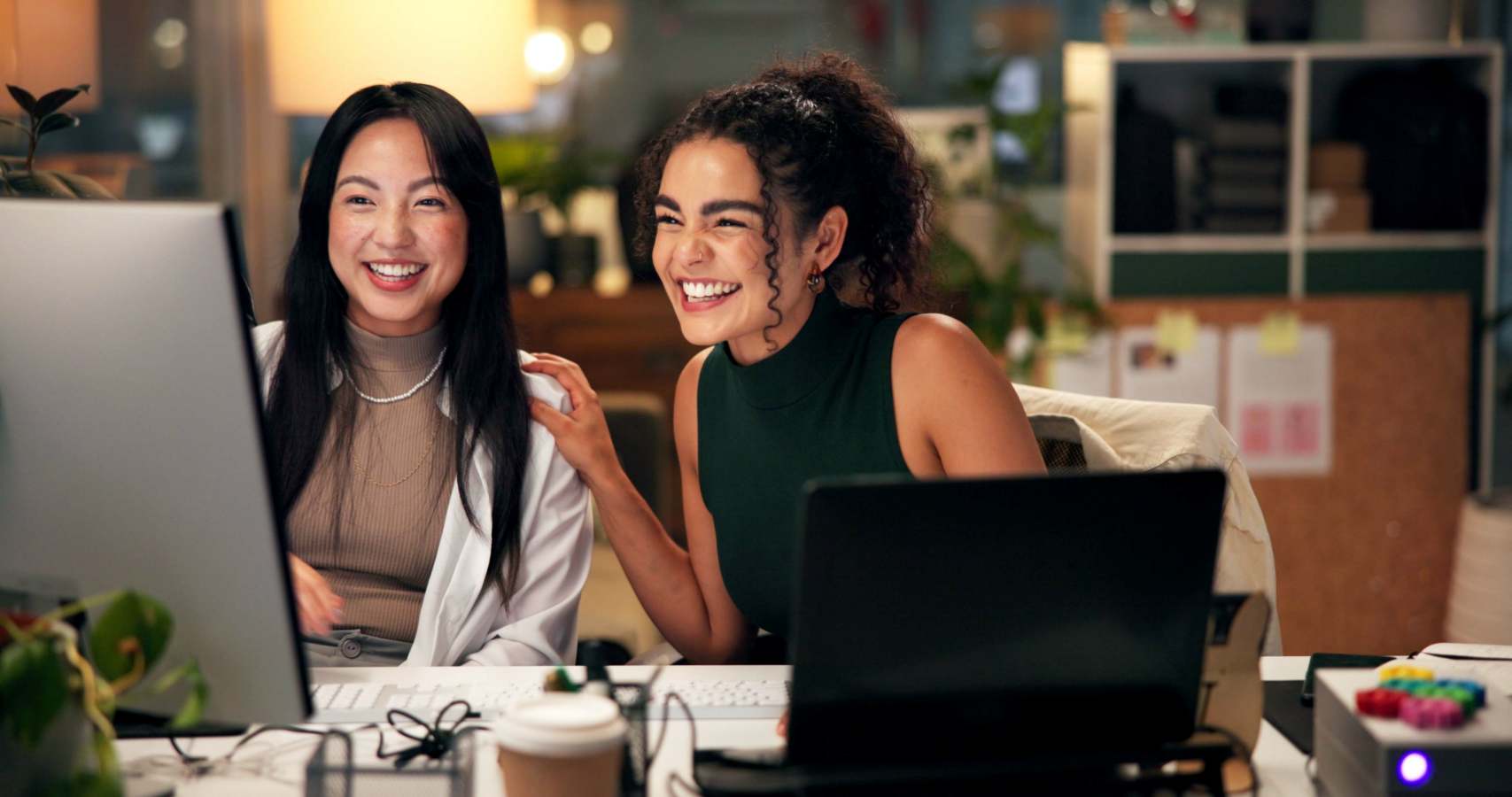 Twee vrouwen lachen samen achter een computerscherm