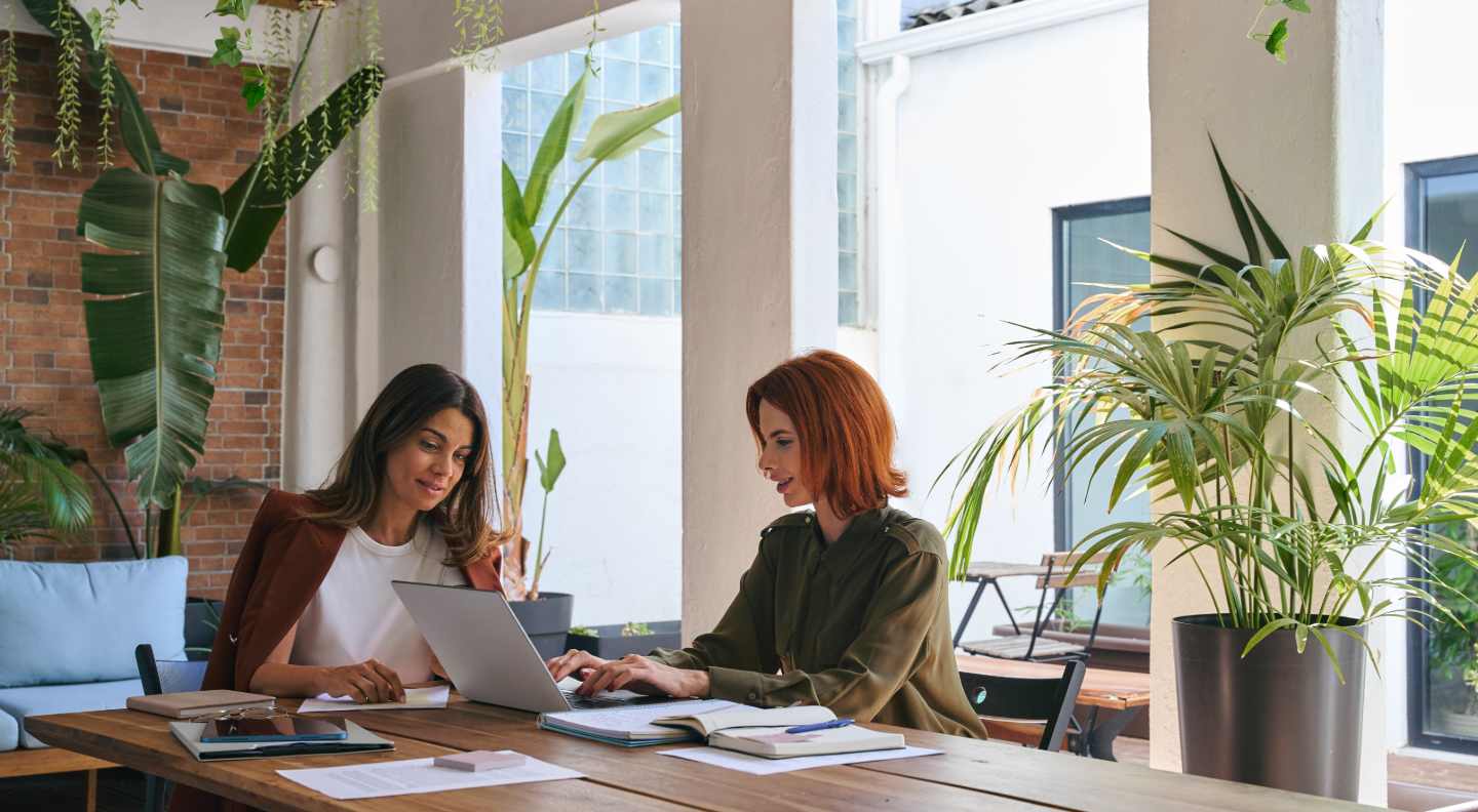 Twee vrouwen werken samen achter een laptop tussen planten