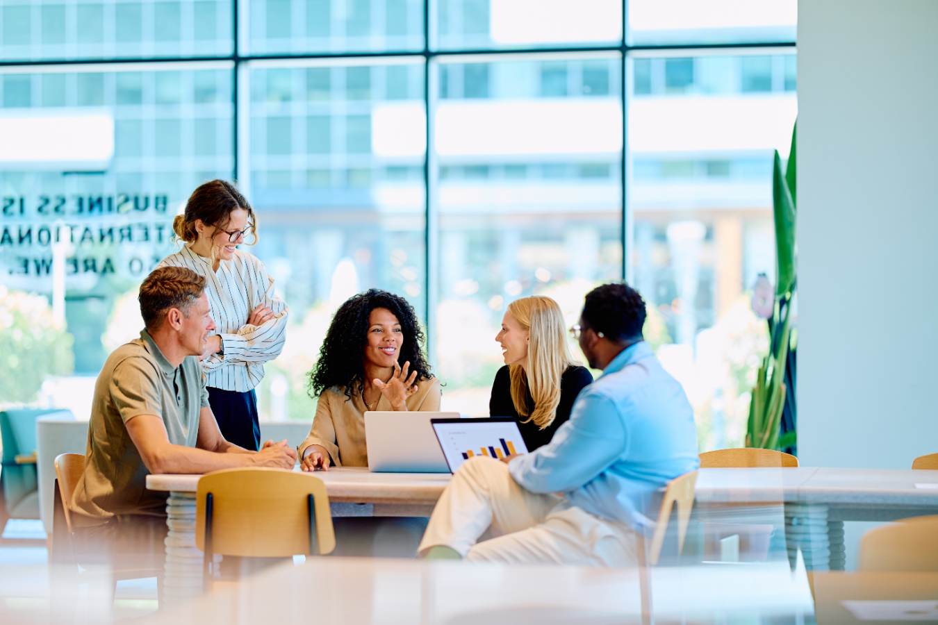Five colleagues having a meeting at a table by a large window