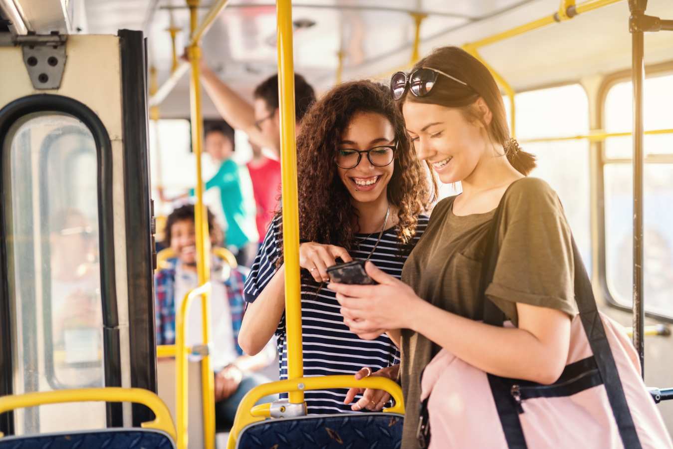 Twee lachende vrouwen kijken samen naar een smartphone in de bus