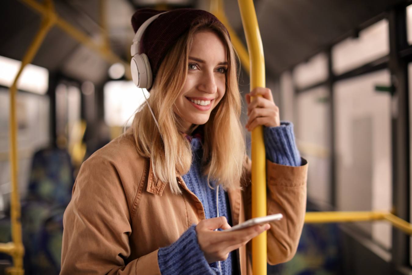 Vrouw met koptelefoon en muts houdt telefoon vast in de bus