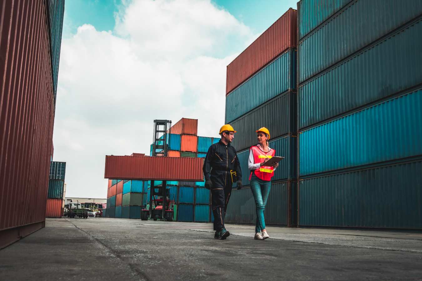 Man en vrouw met helm lopen met tablet tussen vrachtcontainers