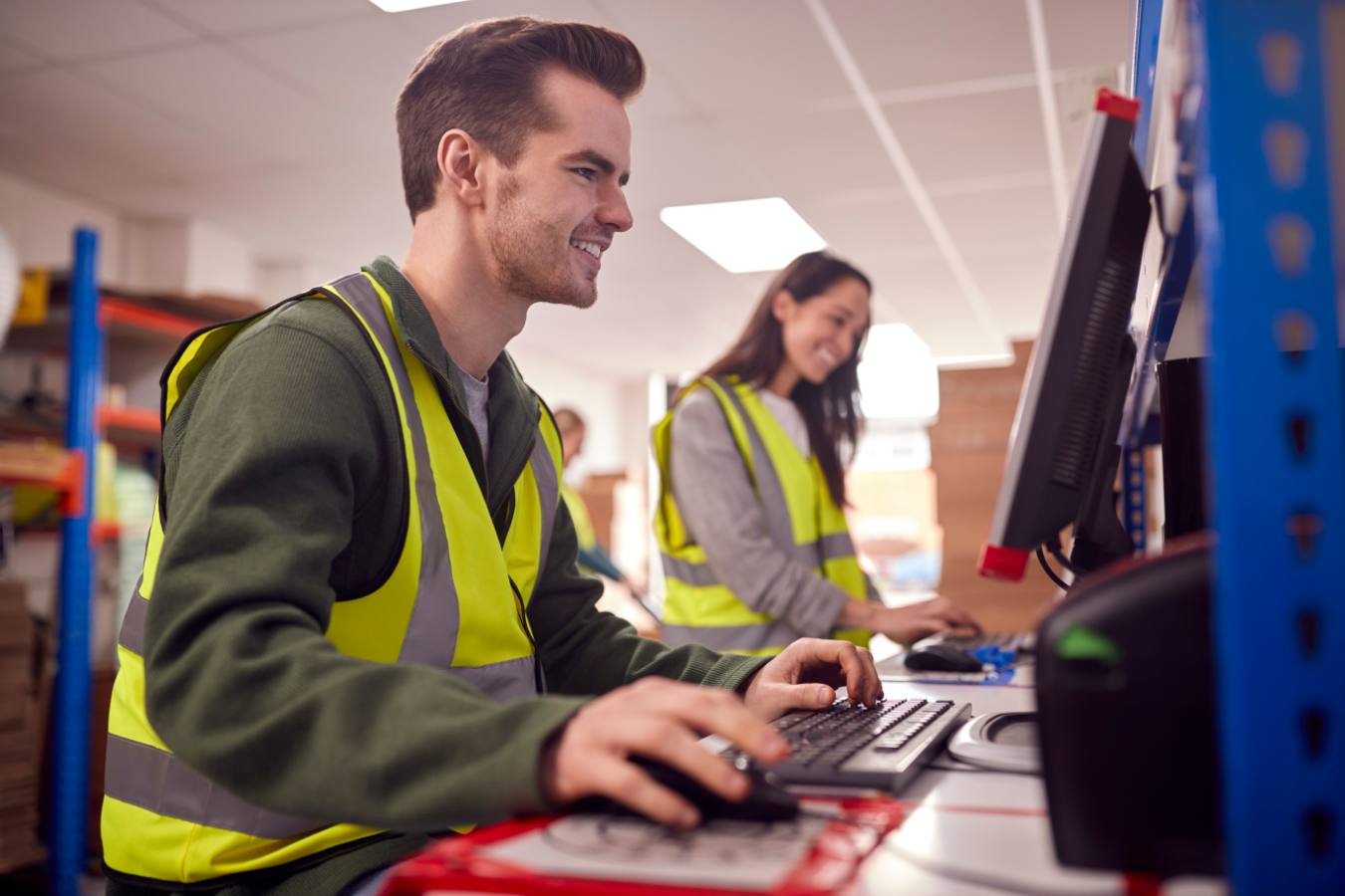 Jonge man met veiligheidshesje werkt achter computer in magazijn